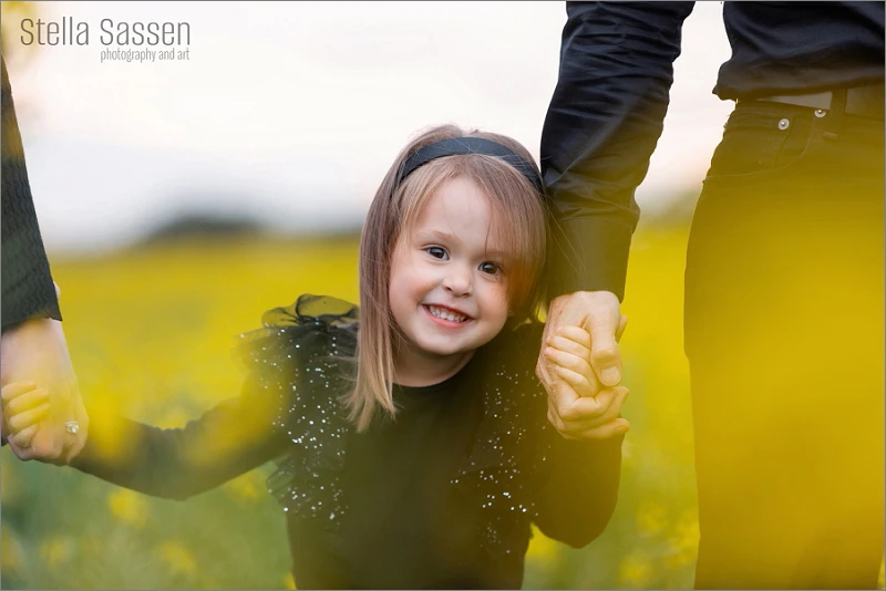 Sweet little girl smiling at the camera during her family shoot in Cape Town, surrounded by yellow canola flowers
